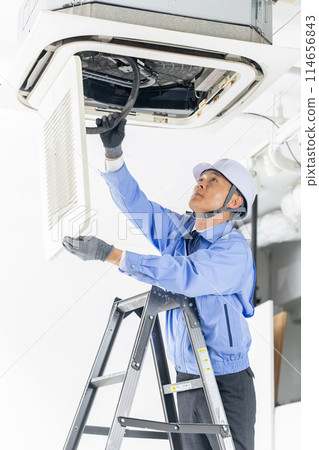 Man in work clothes inspecting air conditioner vertical Man in work clothes inspecting air conditioner vertical 114656843