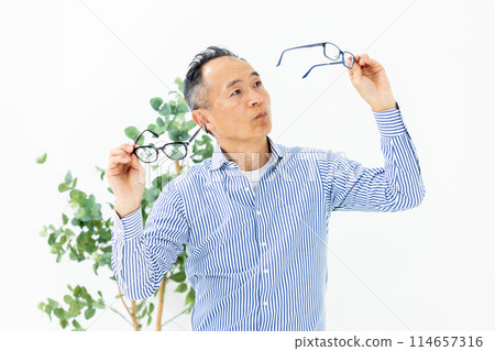 Middle-aged man choosing glasses confused Middle-aged man choosing glasses confused 114657316