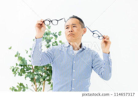 Middle-aged man choosing glasses confused Middle-aged man choosing glasses confused 114657317