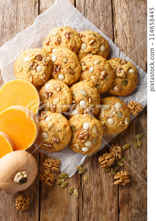 Healthy gluten-free pumpkin cookies with walnuts and seeds close-up on parchment on a wooden table. Vertical top view Healthy gluten-free pumpkin cookies with walnuts and seeds close-up on parchment on a wooden table. Vertical top view 114658445