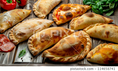 Italian traditional baked calzone with tempting fillings and ingredients on wooden table, food delivery Italian traditional baked calzone with tempting fillings and ingredients on wooden table, food delivery 114658741