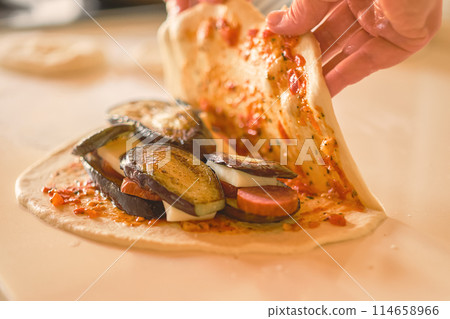 Chef's hands cover ingredients on dough while preparing traditional Italian dish calzone, selective focus and blurred background Chef's hands cover ingredients on dough while preparing traditional Italian dish calzone, selective focus and blurred background 114658966