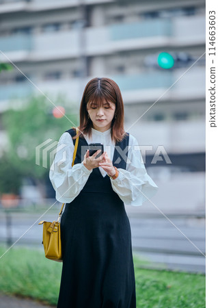 一位年輕女子邊走邊使用智慧型手機 114663603