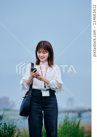 A young woman walking while operating a smartphone A young woman walking while operating a smartphone 114663612