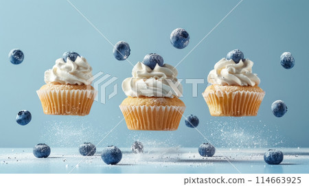 Three cupcakes with blueberry flying in air, powdered sugar and decorated whipped cream on blue pastel gradient background 114663925