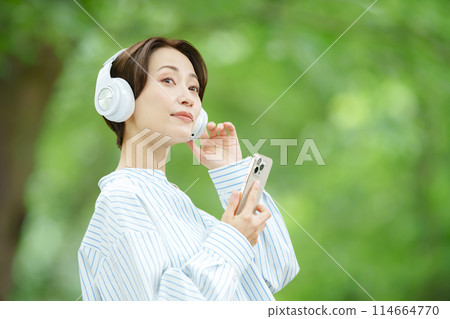 Fresh greenery A woman wearing earphones and holding a smartphone 114664770