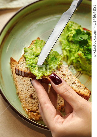 Female hands spreading guacamole on slice of toasted bread Female hands spreading guacamole on slice of toasted bread 114664853