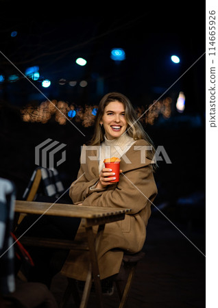 lonely beautiful girl in the evening at a table in a street cafe with a glass of coffee in her hands, night, bokeh 114665926