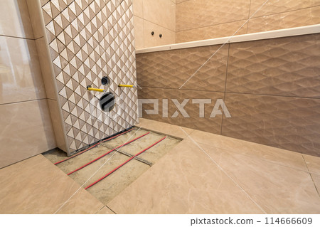 Unfinished reconstruction of bathroom with ceramic tiles installed on walls, heating electrical cables system on cement floor and place for toilet. Unfinished reconstruction of bathroom with ceramic tiles installed on walls, heating electrical cables system on cement floor and place for toilet. 114666609
