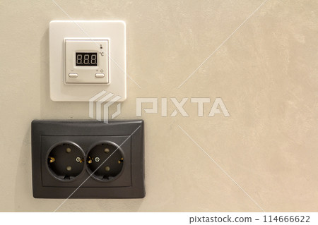 Double electric isolated socket and thermostat installed on light yellow plastered wall. Power supply and temperature regulation, energy saving, comfortable home concept. Double electric isolated socket and thermostat installed on light yellow plastered wall. Power supply and temperature regulation, energy saving, comfortable home concept. 114666622