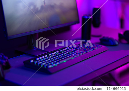 Modern gaming setup with keyboard, mouse, and monitor in a dimly-lit room with purple lighting Modern gaming setup with keyboard, mouse, and monitor in a dimly-lit room with purple lighting 114666913