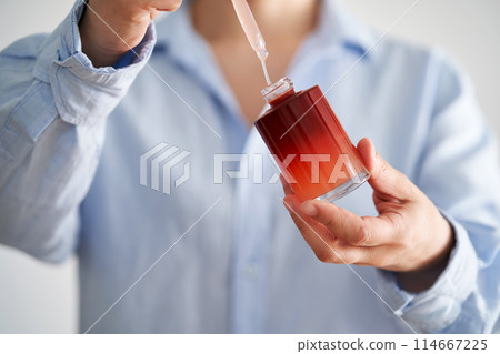Female hands in a blue shirt hold a pink bottle of serum. Female hands in a blue shirt hold a pink bottle of serum. 114667225