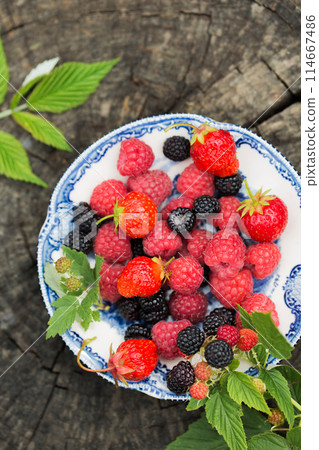 Raspberries, strawberry and wild blackberries on a vintage plate 114667486