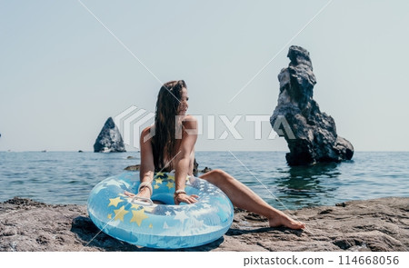 Woman summer sea. Happy woman swimming with inflatable donut on the beach in summer sunny day, surrounded by volcanic mountains. Summer vacation concept. Woman summer sea. Happy woman swimming with inflatable donut on the beach in summer sunny day, surrounded by volcanic mountains. Summer vacation concept. 114668056