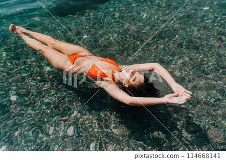 Woman swimming floating in calm sea. Happy smiling woman with long hair and fit body enjoys sea beach during summer vacation holidays. Concept of body image and fitness, enjoying a serene beach. Woman swimming floating in calm sea. Happy smiling woman with long hair and fit body enjoys sea beach during summer vacation holidays. Concept of body image and fitness, enjoying a serene beach. 114668141