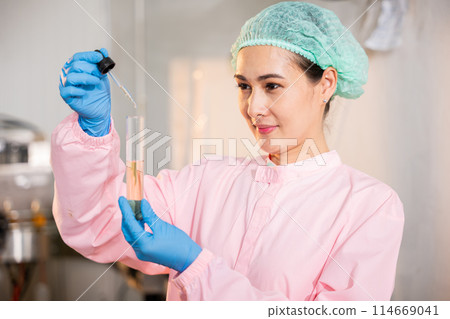 At juice beverage factory woman food engineer executes food and beverage quality and safety testing using test tubes to sample basil or chia seeds in bottled products in laboratory control. 114669041