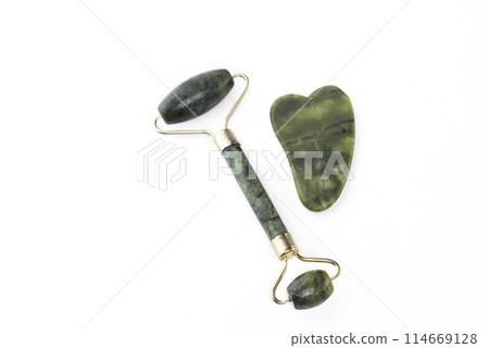 Green face roller and gua sha massager made from natural jade nephritis stone isolated on white background. Facial massage concept Green face roller and gua sha massager made from natural jade nephritis stone isolated on white background. Facial massage concept 114669128
