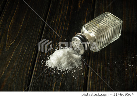 Heap of salt from a salt shaker on a black table. The concept of excessive salt intake that can be the cause of diabetes or other diseases Heap of salt from a salt shaker on a black table. The concept of excessive salt intake that can be the cause of diabetes or other diseases 114669564