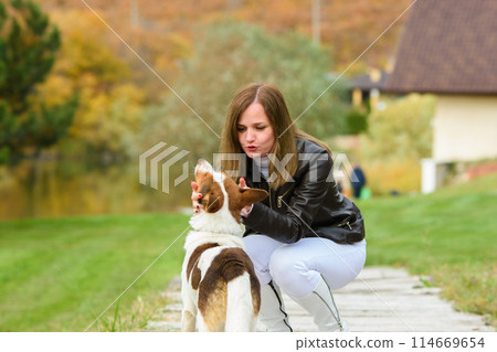 A young beautiful girl caresses a dog, against the backdrop of a beautiful landscape A young beautiful girl caresses a dog, against the backdrop of a beautiful landscape 114669654