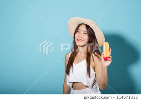 Beautiful Asian young woman holding body lotion on hand in studio shot isolated on blue background, Brunette female hold cream sunblock bottle, tube of sunscreen, Beauty cosmetics facial treatment Beautiful Asian young woman holding body lotion on hand in studio shot isolated on blue background, Brunette female hold cream sunblock bottle, tube of sunscreen, Beauty cosmetics facial treatment 114671318