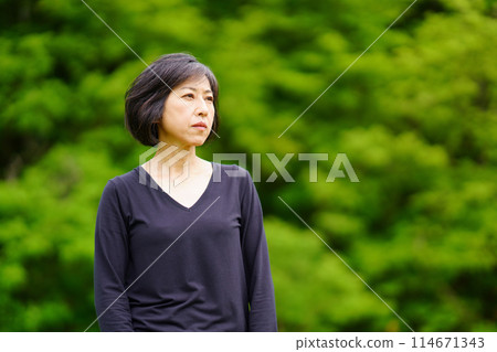 A middle-aged woman wearing black clothes standing lonely among the greenery A middle-aged woman wearing black clothes standing lonely among the greenery 114671343