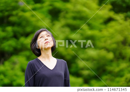 一位身穿黑衣的中年婦女孤獨地站在綠叢中 114671345