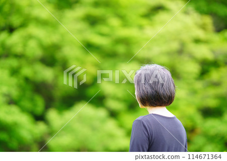 Back view of a middle-aged woman wearing black clothes standing in the greenery Back view of a middle-aged woman wearing black clothes standing in the greenery 114671364