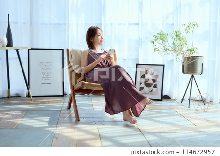 A woman sitting on a chair in a room and looking at her smartphone 114672957