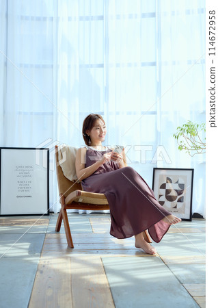 A woman sitting on a chair in a room and looking at her smartphone 114672958