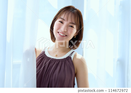 A woman relaxing in a room through lace curtains 114672972
