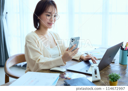 一位女士在家一邊工作一邊看智慧型手機 114672997