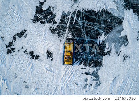 Aerial top down view on a hovercraft parked on the beautiful cracked ice of the lake Baikal. Winter Baikal, frozen lake. Amazing winter landscape. Aerial top down view on a hovercraft parked on the beautiful cracked ice of the lake Baikal. Winter Baikal, frozen lake. Amazing winter landscape. 114673056