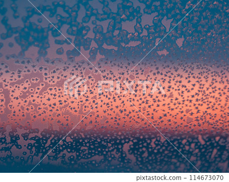 Frozen window with frost patterns overlooking colorful sunset in winter evening Frozen window with frost patterns overlooking colorful sunset in winter evening 114673070