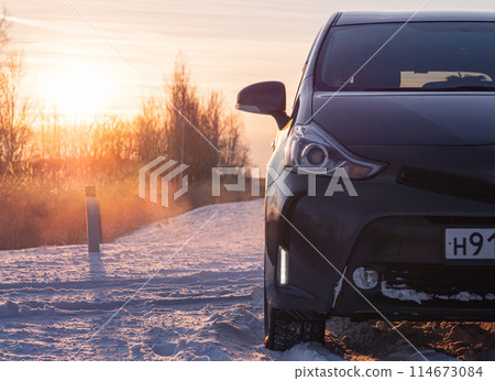 Dark gray car parked on snowy road at sunrise in winter countryside 114673084