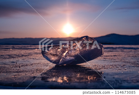 Ice crystal on the frozen surface of Lake Baikal in early morning. Sky and sun reflections on the ice surface. Amazing winter landscape. Winter tourist season at lake Baikal 114673085
