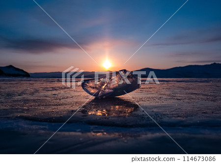 Ice crystal on the frozen surface of Lake Baikal in early morning. Sky and sun reflections on the ice surface. Amazing winter landscape. Winter tourist season at lake Baikal 114673086
