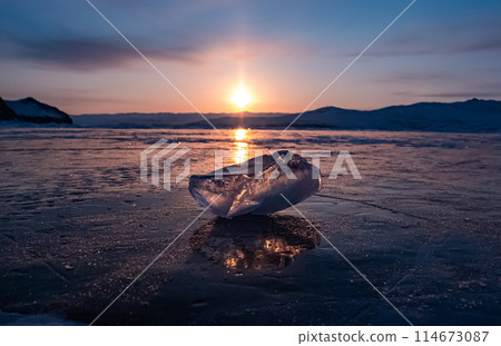 Ice crystal on the frozen surface of Lake Baikal in early morning. Sky and sun reflections on the ice surface. Amazing winter landscape. Winter tourist season at lake Baikal 114673087