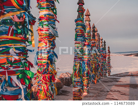Traditional buryat shaman sacred pillars with colorful ribbons in winter at sunset, cape Burkhan, Olkhon island. Winter Baikal. 114673089