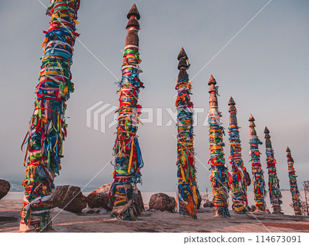 Traditional buryat shaman sacred pillars with colorful ribbons in winter at sunset, cape Burkhan, Olkhon island. Winter Baikal. Traditional buryat shaman sacred pillars with colorful ribbons in winter at sunset, cape Burkhan, Olkhon island. Winter Baikal. 114673091