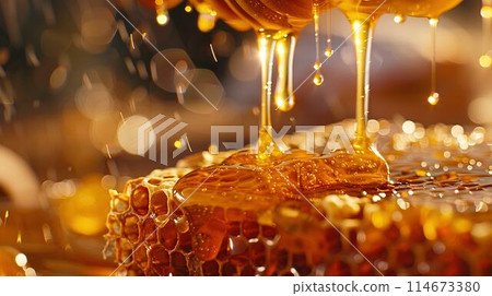 Honey dripping from the wooden honey dropper over thick golden honeycomb on a blurred background. A close up view of the natural organic sweet product. 114673380