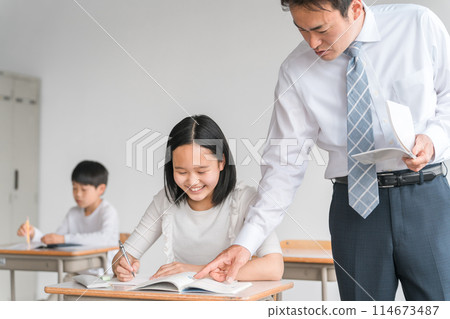Smiling elementary and junior high school students (girls) asking questions to a male teacher, cram school instructor, or teacher teaching while looking at a textbook 114673487