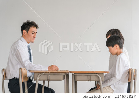 Worried parent and child (elementary school student / boy) who has a three-way interview / individual interview with a male teacher in a school classroom 114675827