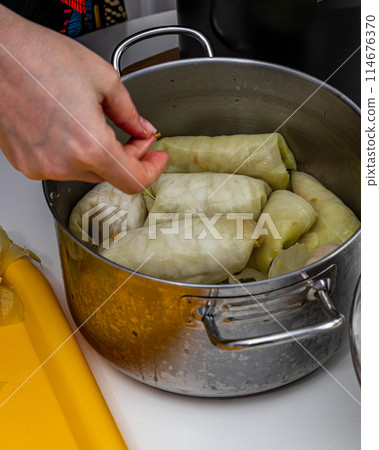 A woman cooks cabbage rolls over a pan at home. 114676370
