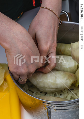 Women cook cabbage rolls while standing at the table and put them in a pot. 114676374