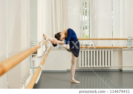 Dancer stretching leg muscles, bending her body forward and pressing her head to her knee 114679431