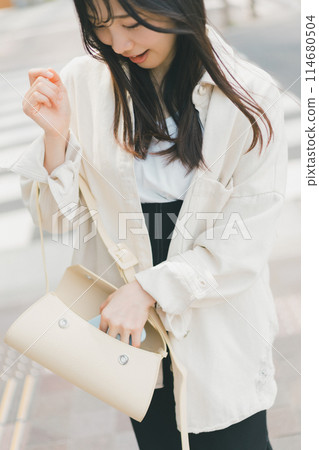 A young woman walking down the street taking out a smartphone from her bag A young woman walking down the street taking out a smartphone from her bag 114680504