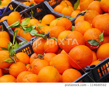A crate full of oranges with some of them having green leaves on them A crate full of oranges with some of them having green leaves on them 114680582