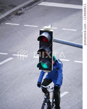 A man is riding a bike down a street with a green light at a traffic light 114680611