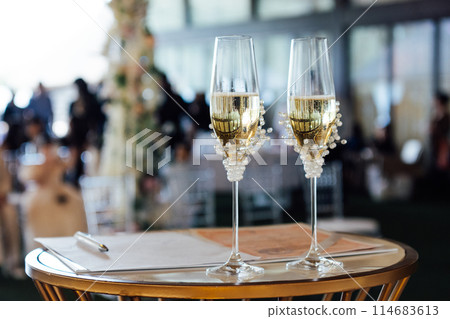 Two wedding glasses stand on a stand against the backdrop of the ceremony arch. 114683613