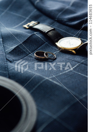Groom's wedding details. Watch, rings and belt placed on a checkered jacket 114683655